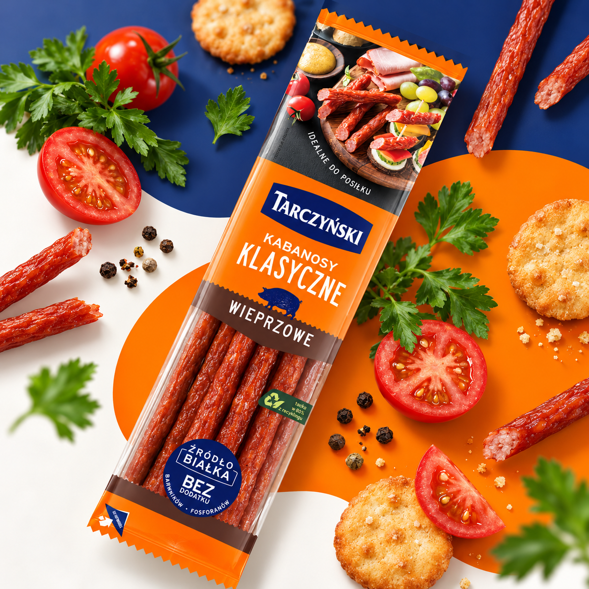 Tarczyński Kabanosy Klasyczne Wieprzowe 300 g mit Tomaten, Petersilie und Crackern vor orange-blauem Hintergrund.